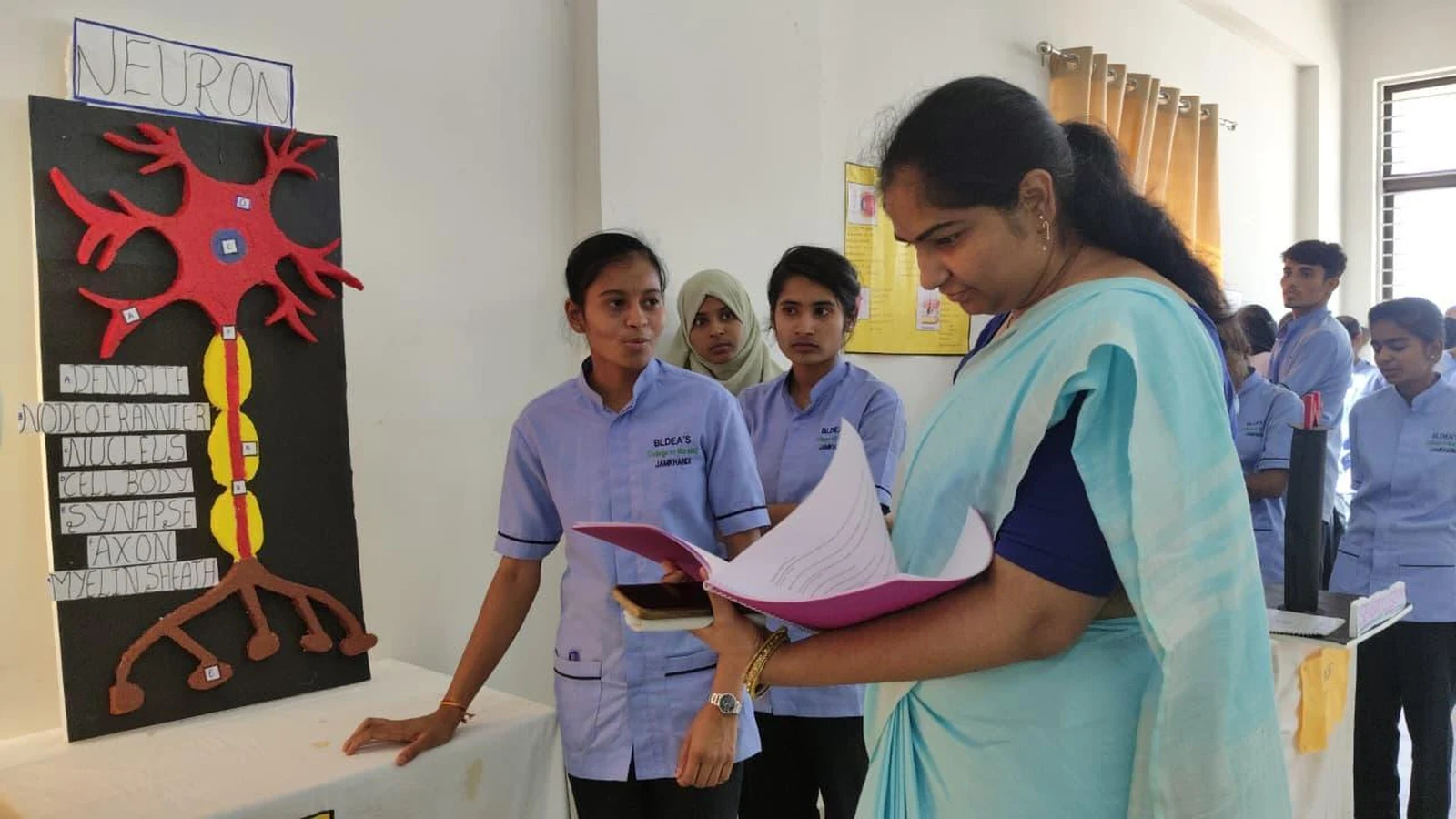 Faculty evaluating Neuron model at Nervous System group presentation – Anatomy Physiology Model Exhibition 2026, BLDEA College of Nursing Jamkhandi