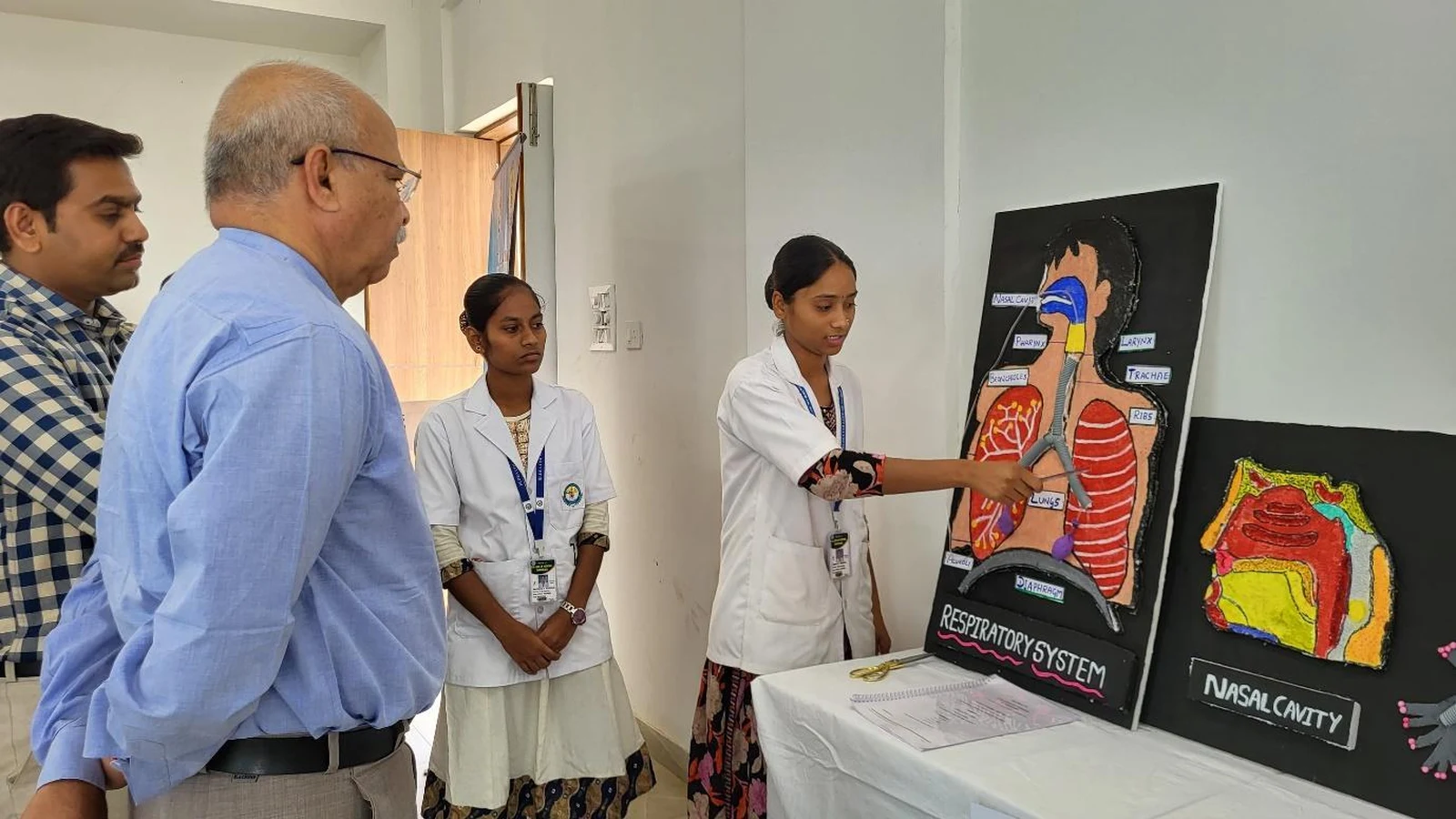 First semester BSc Nursing students of BLDEAS College of Nursing Jamkhandi standing with anatomy and physiology models on display tables during welcome address by Ms Pooja Hosakoti UG Nursing Tutor at Anatomy and Physiology Model Exhibition March 21 2025 with Respiratory System and other models visible