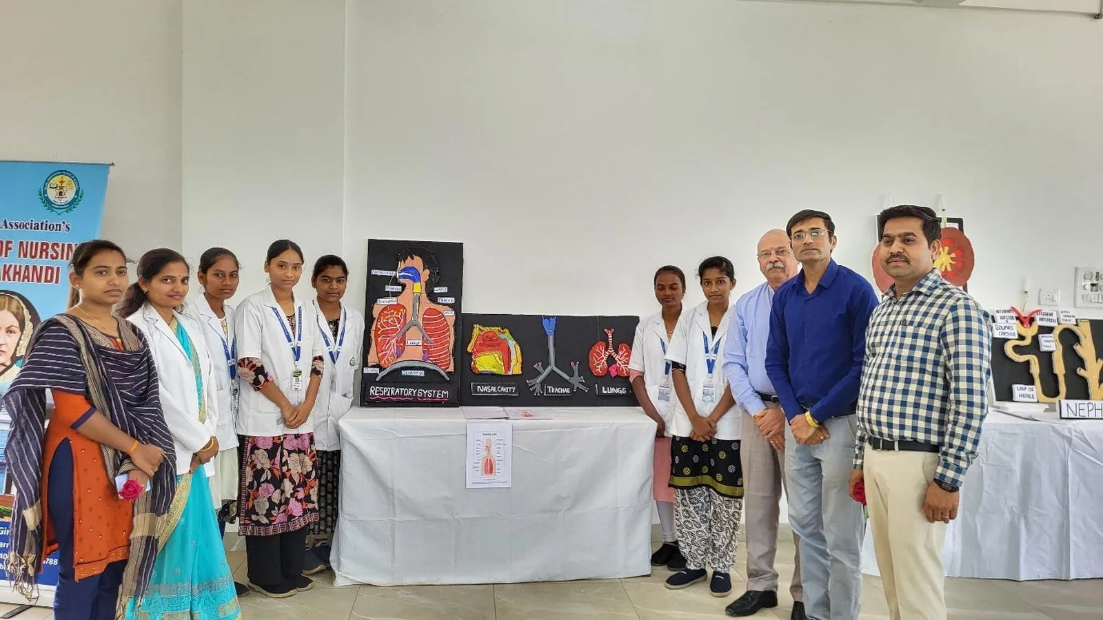 First semester BSc Nursing students presenting Group 1 Respiratory System anatomy model with labeled Trachea Bronchi and Lungs chart to Dr Veeranna S Jatti and faculty judges at Anatomy and Physiology Model Exhibition BLDEAS College of Nursing Jamkhandi March 21 2025