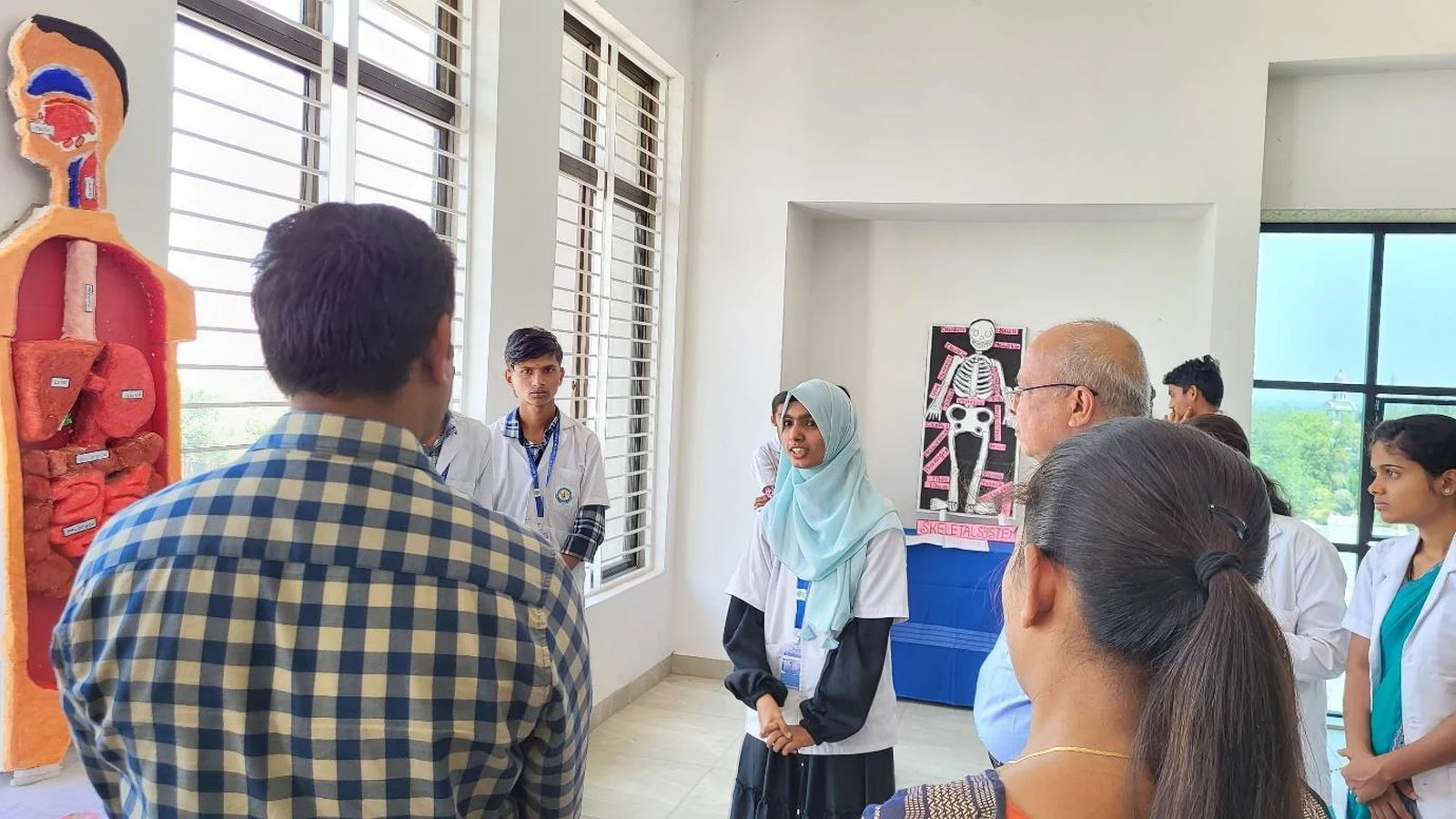 BSc Nursing student from BLDEAS College of Nursing Jamkhandi presenting Group 4 Digestive System anatomy model featuring full body anatomical mannequin with digestive organs in red and orange at Anatomy and Physiology Model Exhibition March 21 2025 with DIGESTIVE SYSTEM label on table