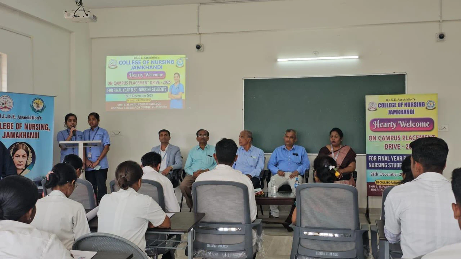 Wide view of Campus Placement Drive 2025 programme at BLDEA College of Nursing Jamkhandi with dignitaries and interview panel seated at front and final year BSc Nursing students seated facing them with placement drive banner projected on screen December 2025