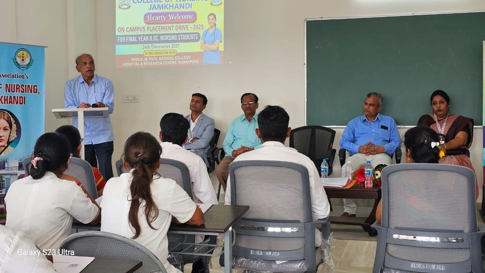 Distinguished dignitary addressing final year BSc Nursing students at podium during Campus Placement Drive 2025 at BLDEA College of Nursing Jamkhandi with interview panel and faculty seated alongside placement drive banner on screen December 2025