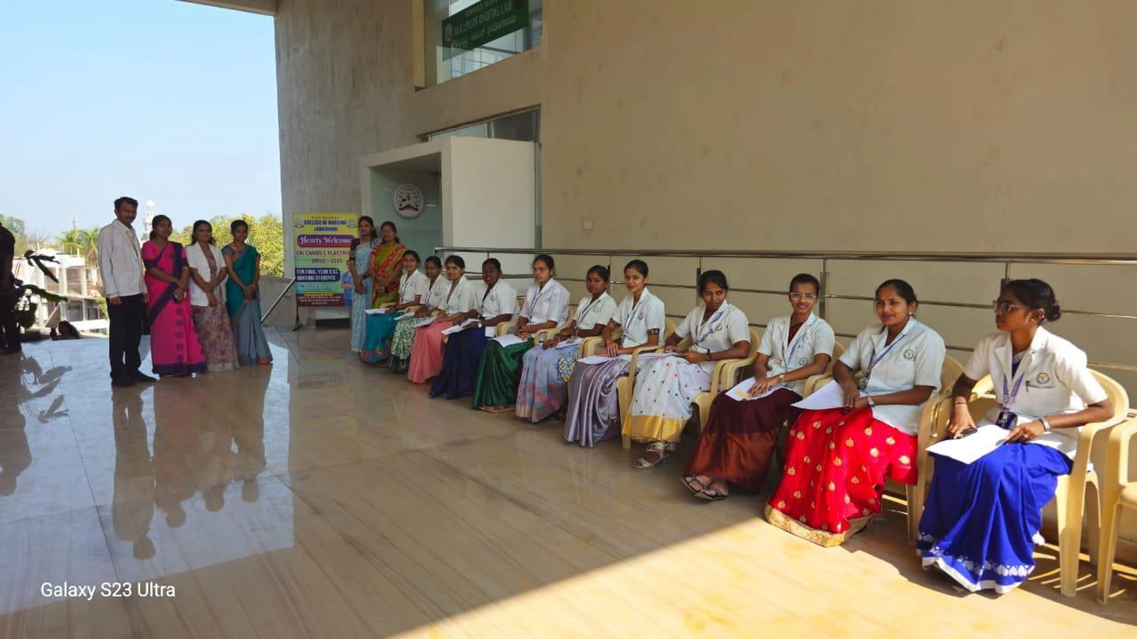 Final year BSc Nursing students in white uniform and traditional dress waiting in college corridor for personal interview at Campus Placement Drive 2025 BLDEA College of Nursing Jamkhandi with placement drive poster visible on stand December 24 2025