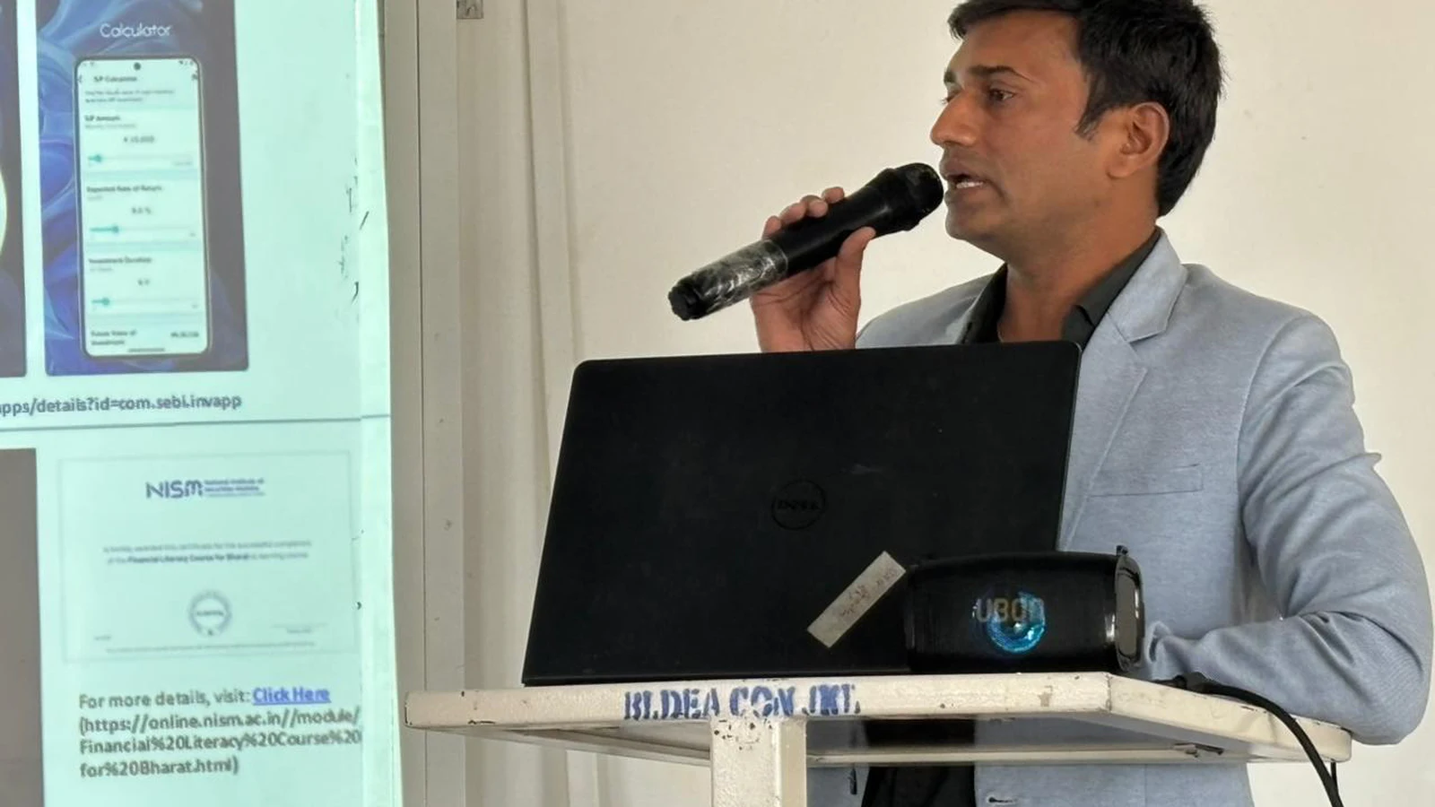 Resource person at BLDEA College of Nursing podium presenting on NISM financial literacy course and investment tools at seminar Jamkhandi