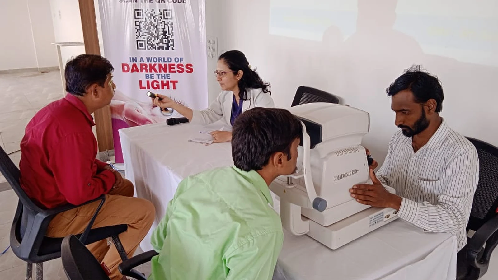 Wide view of free eye screening station during Free Eye Screening Camp September 4 2024 at BLDEAS College of Nursing Jamkhandi Seminar Hall showing MM Joshi Eye Institute team with G-Matronix K30 Plus auto-refractometer examining multiple students and faculty in collaboration with BLDEAS College of Nursing Jamkhandi with SGM eyebank Pledge Your Eyes Online banner visible