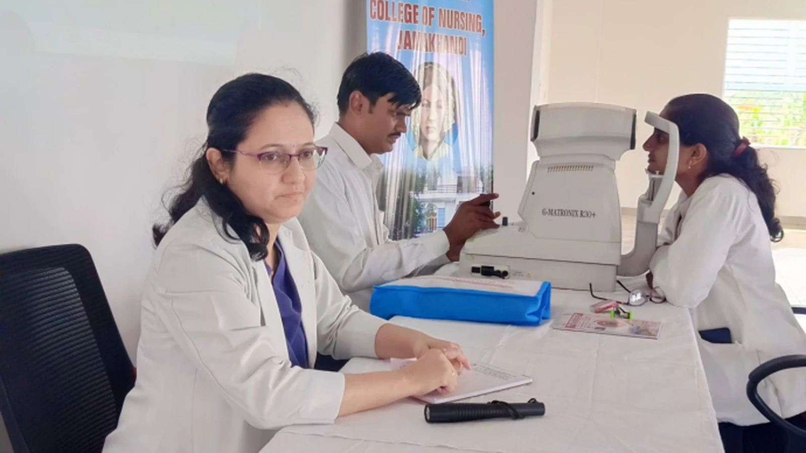 Dr Deepa Udagatti Consultant Ophthalmologist MM Joshi Eye Institute Jamkhandi seated at screening table with MM Joshi Eye Institute optometry technician and BLDEAS College of Nursing Jamkhandi student during Free Eye Screening Camp September 4 2024 Seminar Hall BLDEAS College of Nursing Jamkhandi with BLDEA Association College of Nursing Jamkhandi banner visible in background