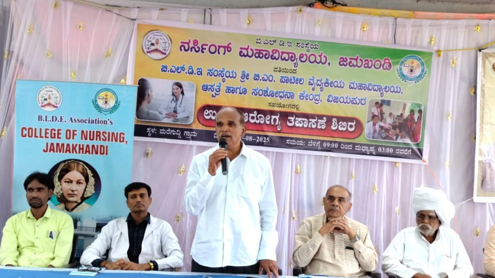 Shri AM Shah President College Development Committee and Prof SH Lagali with dignitaries seated on dais at free health check-up camp organized by BLDEAS College of Nursing Jamkhandi with Shri BM Patil Medical College Vijayapura at Mareguddi village August 1 2025