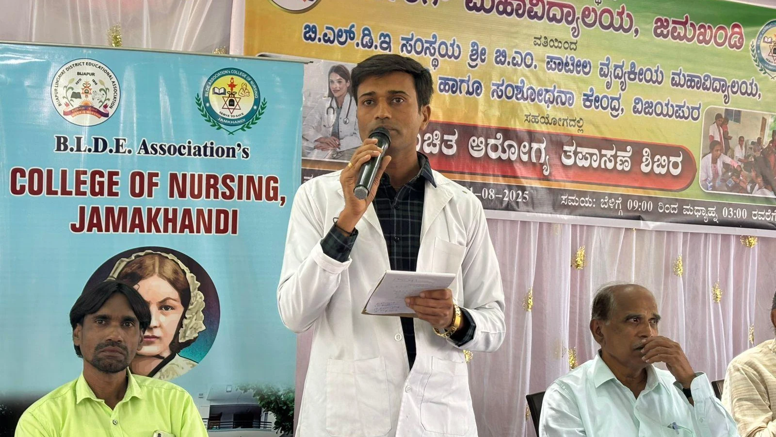 Dr Veerabhadrappa G Mendagudli Principal BLDEAS College of Nursing Jamkhandi delivering welcome address at free health check-up camp at Mareguddi village Karnataka August 1 2025 with health camp event banner visible in background