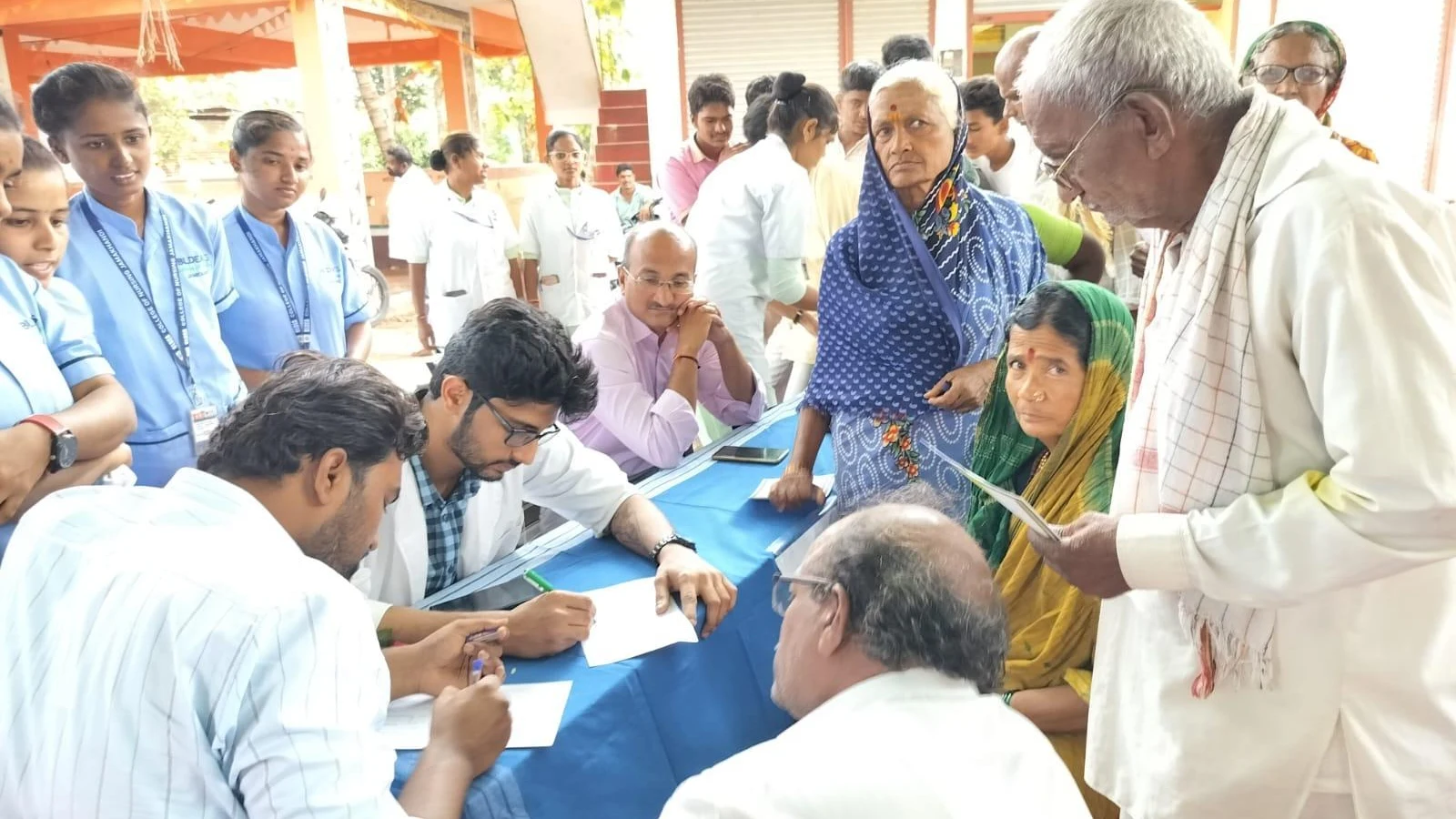 Wide view of free health check-up camp with multiple consultation tables attended by nursing students doctors and medical staff of BLDEAS College of Nursing Jamkhandi serving villagers of Mareguddi in collaboration with Shri BM Patil Medical College Vijayapura August 1 2025