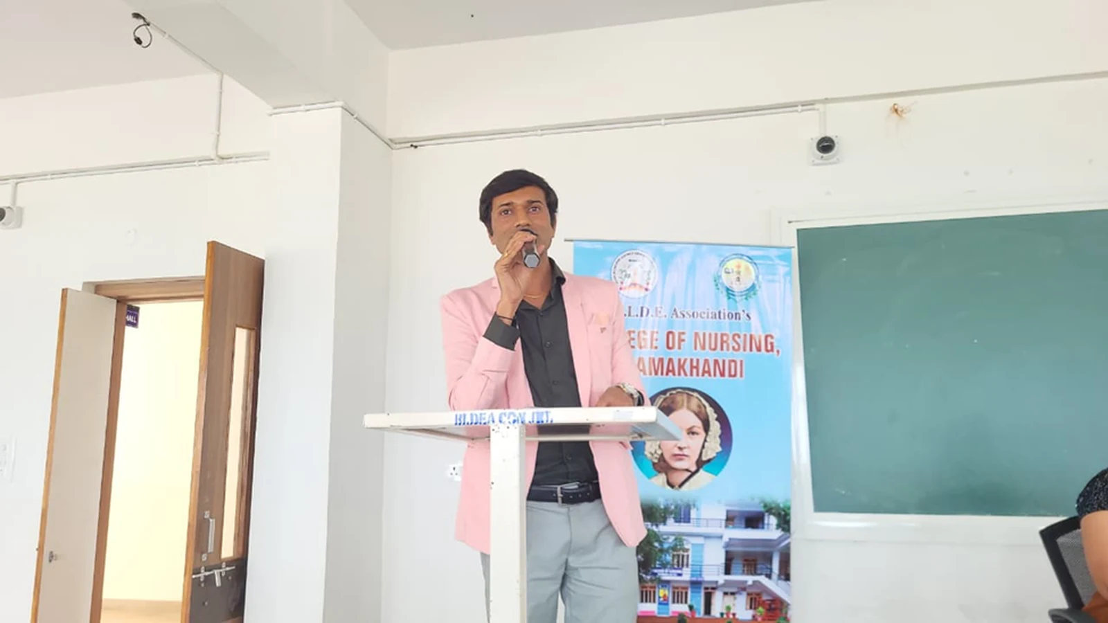 Faculty member addressing audience at podium during guest lecture on Blood Cancer Challenges Prevention and Nursing Responsibilities at BLDEA College of Nursing Jamkhandi October 15 2025