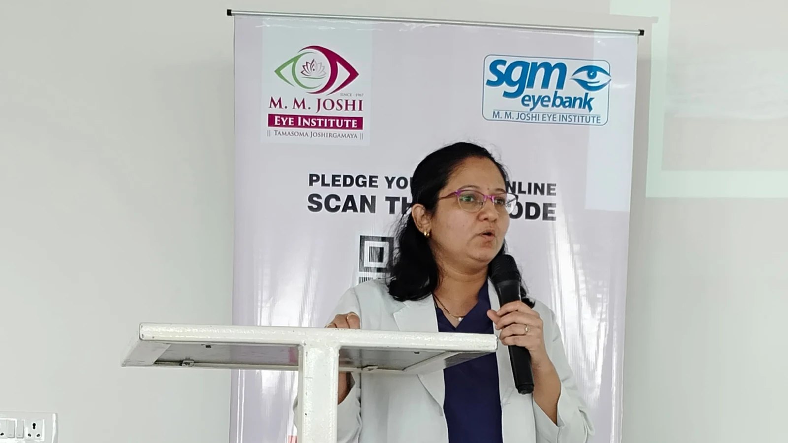 Close view of Dr Deepa Udagatti Consultant Ophthalmologist MM Joshi Eye Institute Jamkhandi speaking at guest lecture on Eye Care and Eye Donation Awareness organized by BLDEAS College of Nursing Jamkhandi on National Eye Donation Week September 4 2024 with MM Joshi Eye Institute SGM eyebank Pledge Your Eyes Online banner in background