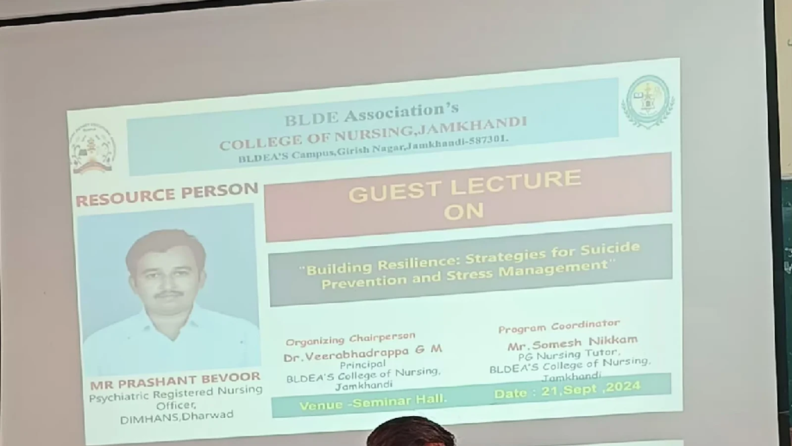 Mr Prashant Bevoor Psychiatric Registered Nursing Officer DIMHANS Dharwad delivering guest lecture on Building Resilience Strategies for Suicide Prevention and Stress Management at Seminar Hall BLDEAS College of Nursing Jamkhandi September 21 2024 holding microphone with event poster projected on screen behind him