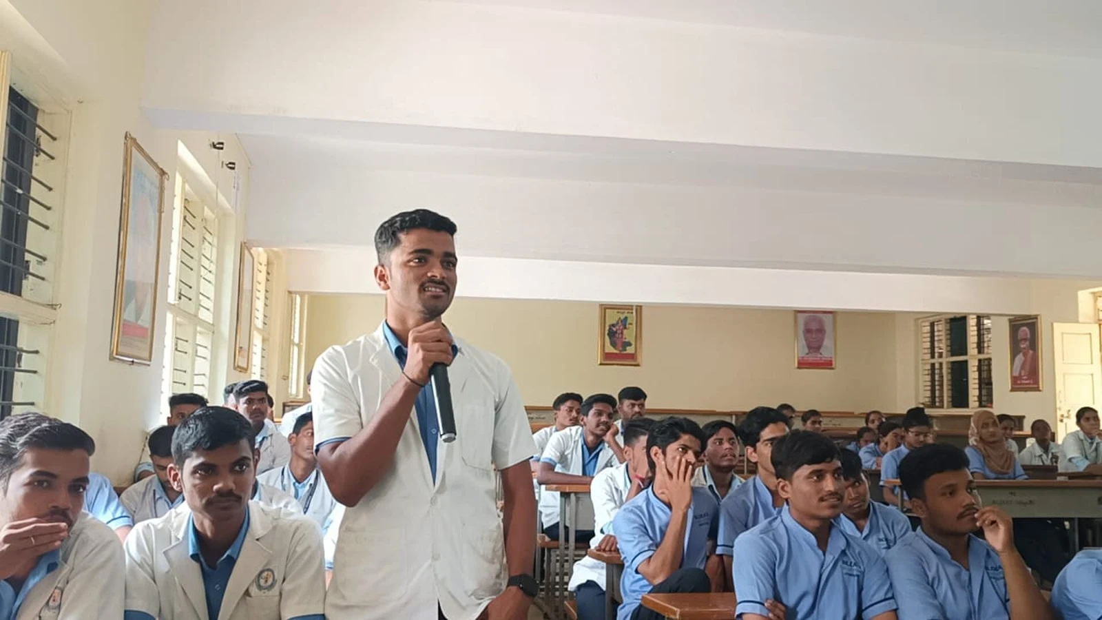 BSc Nursing student of BLDEAS College of Nursing Jamkhandi standing with microphone participating in interactive question and answer session during guest lecture on Building Resilience Strategies for Suicide Prevention and Stress Management by Mr Prashant Bevoor DIMHANS Dharwad at BLDEAS College of Nursing Jamkhandi September 21 2024 with fellow students seated in background