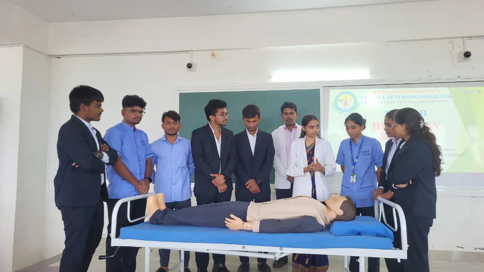 Nursing students from BLDEAS College of Nursing Jamkhandi demonstrating CPR technique on mannequin on hospital bed to BBA students gathered around during hands-on CPR training session for World Heart Day 2025