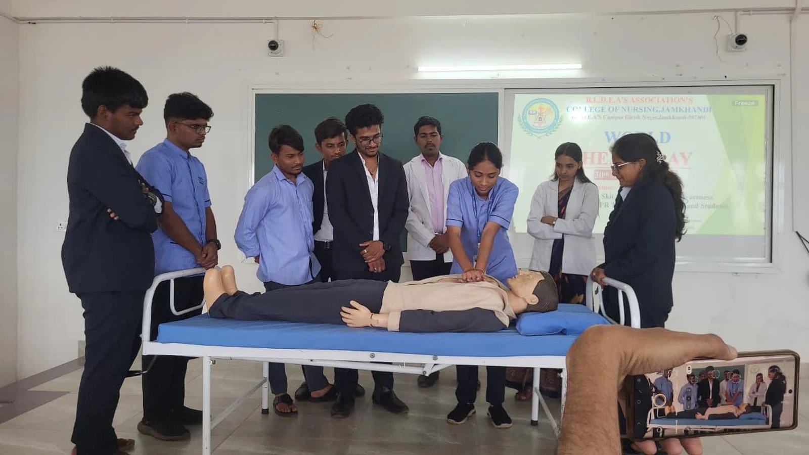 Student performing CPR chest compression on mannequin on hospital bed while participants watch during hands-on CPR training for World Heart Day 2025 organized by BLDEAS College of Nursing Jamkhandi at BLDE BBA Seminar Hall September 30 2025