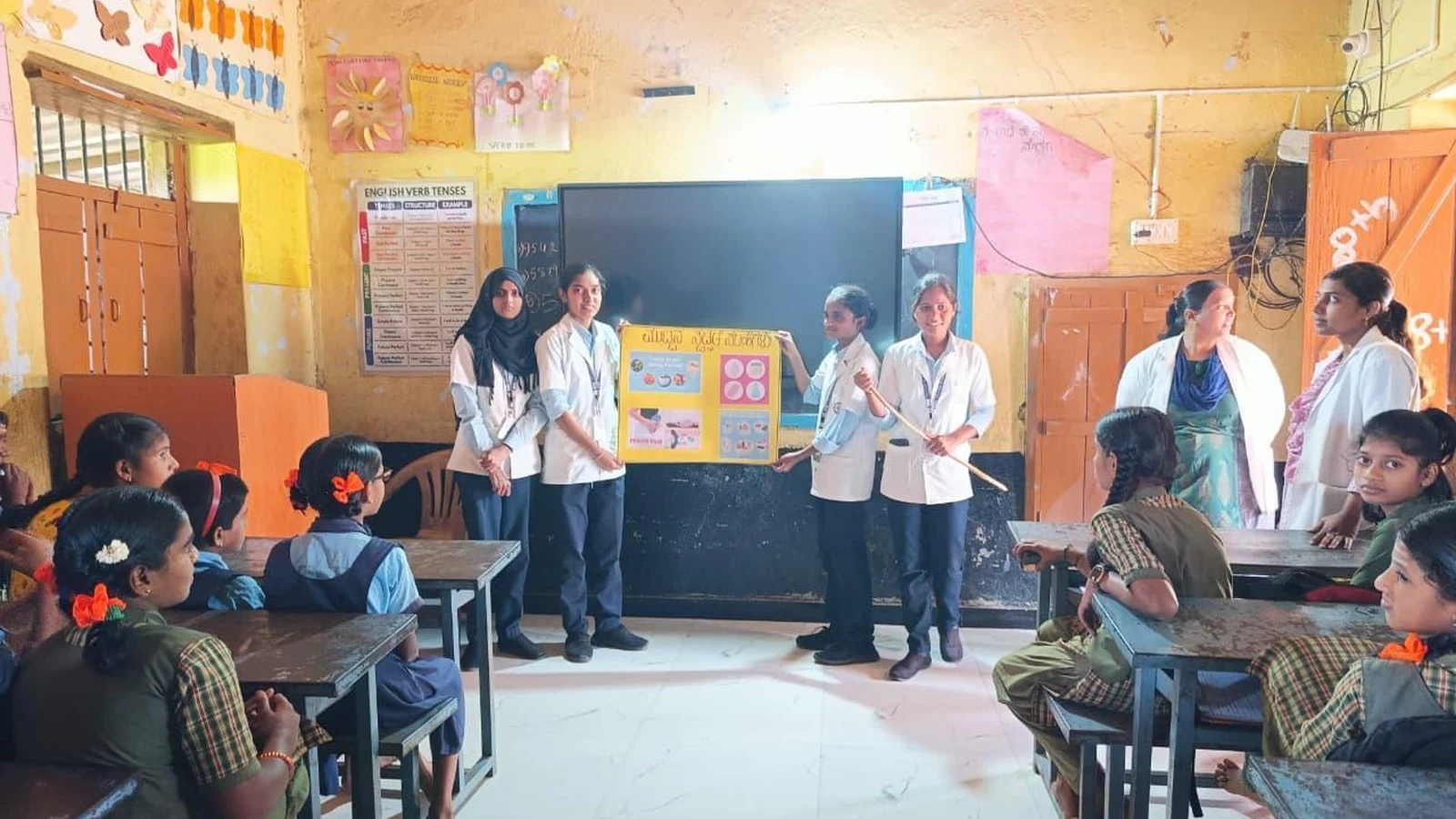 BLDEA College of Nursing Jamkhandi Seventh Semester BSc Nursing students conducting menstrual hygiene education session with chart for adolescent girls at Government Primary School Kakanwadi Village June 2026