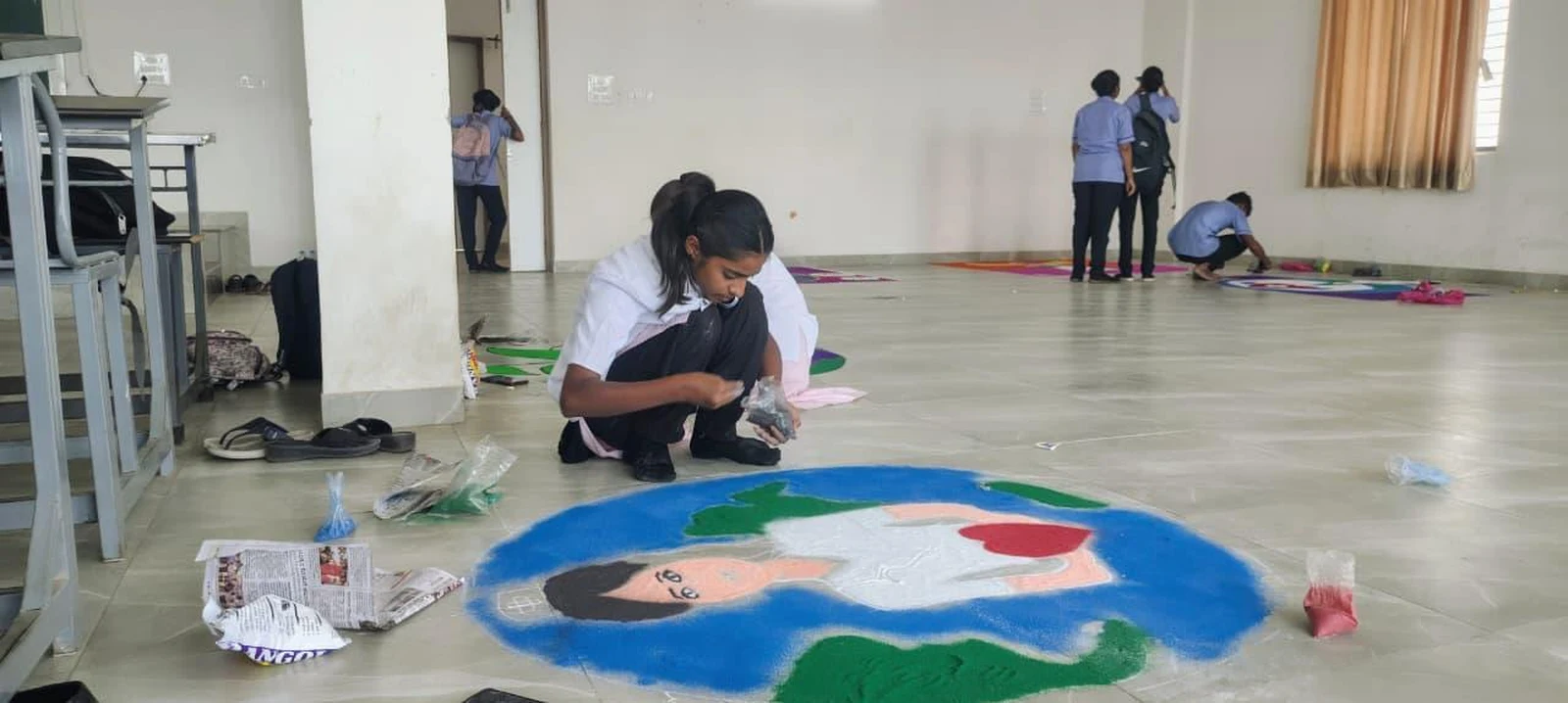 Student working on globe and nurse rangoli at Intercollegiate Rangoli Competition 2026 – BLDEA College of Nursing Jamkhandi