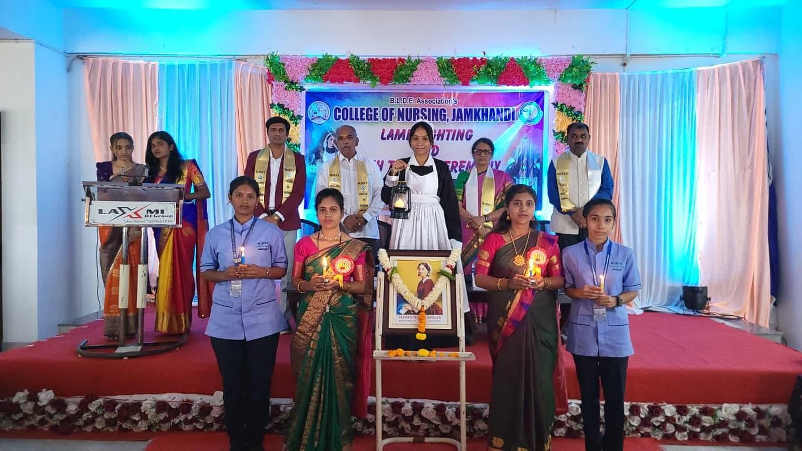 Students and faculty on stage during Lamp Lighting Ceremony with Florence Nightingale portrait at BLDEA College of Nursing Jamkhandi 2026