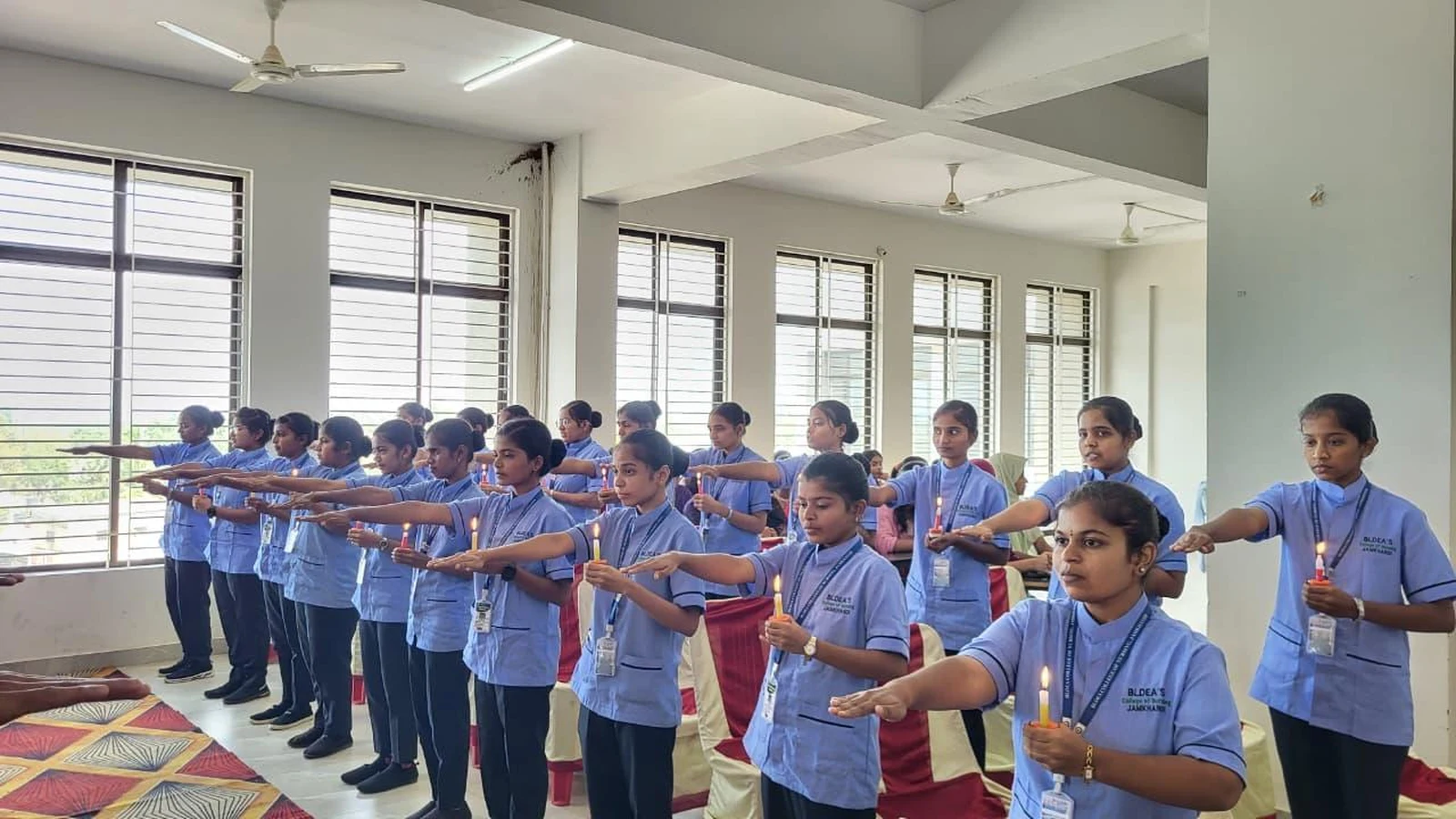 1st Year BSc Nursing students in blue uniform holding lighted candles in rows during Oath Taking Ceremony at Lamp Lighting and Oath Taking Ceremony 2025 BLDEA College of Nursing Jamkhandi October 25 2025