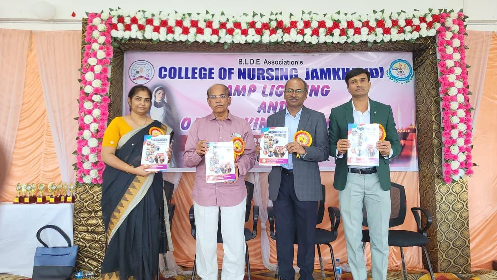 Dignitaries releasing Annual College Magazine Nightingale Chronicles Volume 3 2023-2024 at Lamp Lighting and Oath Taking Ceremony 2025 BLDEA College of Nursing Jamkhandi with ceremony banner and flower-decorated arch October 25 2025