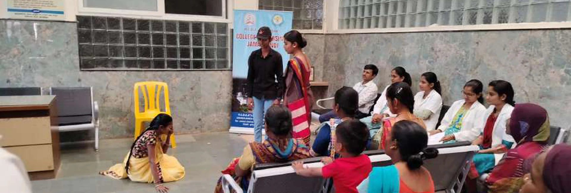 First semester BSc Nursing student in yellow saree performing National Girl Child Day awareness skit before ANC and PNC mothers seated in waiting area at Tungal Hospital Jamkhandi organized by BLDEAS College of Nursing Jamkhandi January 24 2024