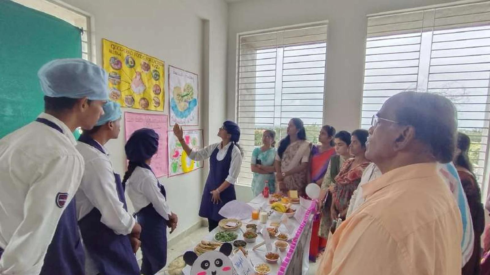 Second semester BSc Nursing student of BLDEAs College of Nursing Jamkhandi in blue uniform presenting diet during lactation chart and diet plan to faculty judges and visitors at their exhibition stall with Good Bad Foods for Lactation Breastfeeding posters on wall during judging session at Nutrition Exhibition and Demonstration Programme 2024 at Nutrition Lab BLDEAs College of Nursing Jamkhandi September 11 2024
