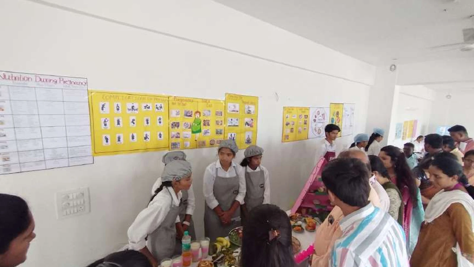 Wide view of Nutrition Exhibition and Demonstration Programme 2024 at Nutrition Lab BLDEAs College of Nursing Jamkhandi September 11 2024 showing multiple diet exhibition stalls with second semester BSc Nursing students in aprons presenting to faculty judges and visitors with Nutrition During Pregnancy charts and posters on walls and various food items and diet plans displayed on tables