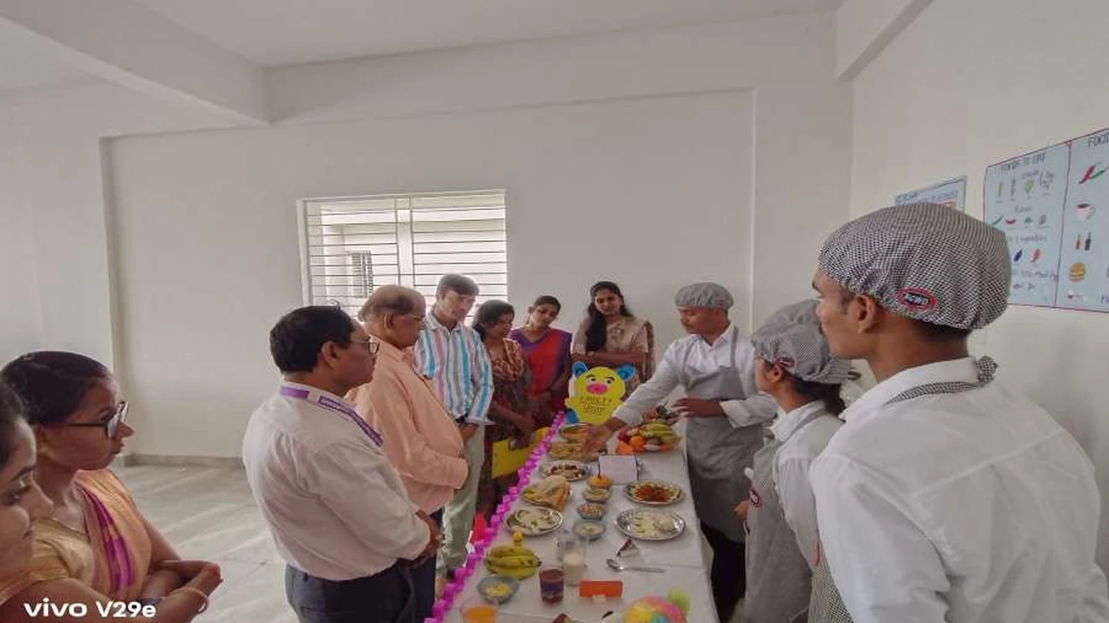 Faculty judges and dignitaries of BLDEAs College of Nursing Jamkhandi evaluating a student diet exhibition stall with second semester BSc Nursing students in grey aprons presenting their diet plan and food items with Food To Live chart visible on wall during judging session at Nutrition Exhibition and Demonstration Programme 2024 at Nutrition Lab BLDEAs College of Nursing Jamkhandi September 11 2024