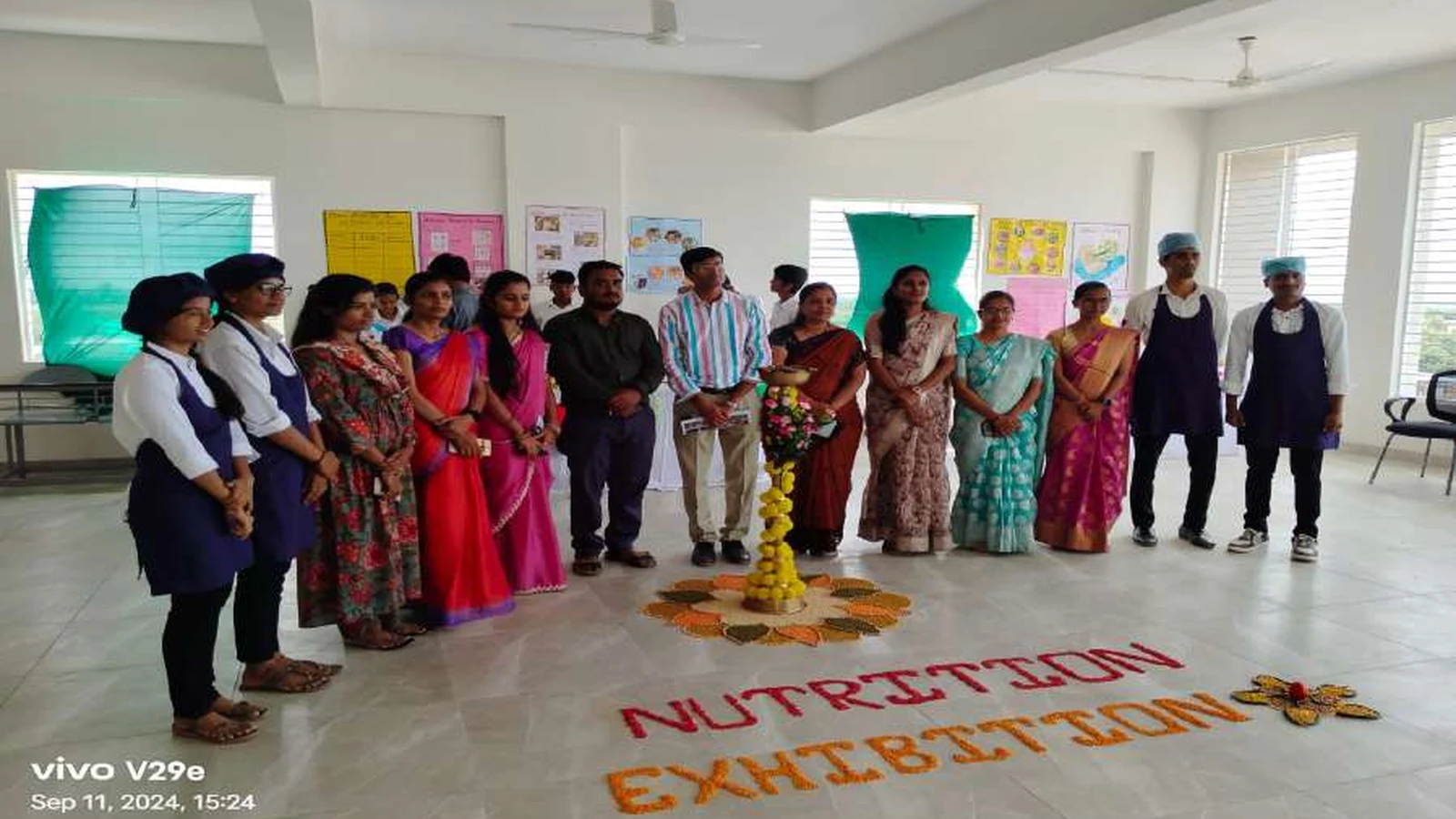 Group photograph of faculty coordinators and second semester BSc Nursing students of BLDEAs College of Nursing Jamkhandi with dignitaries taken at conclusion of Nutrition Exhibition and Demonstration Programme 2024 at Nutrition Lab BLDEAs College of Nursing Jamkhandi on September 11 2024 with NUTRITION EXHIBITION text made from seeds and spices visible on floor and decorative lamp rangoli in centre