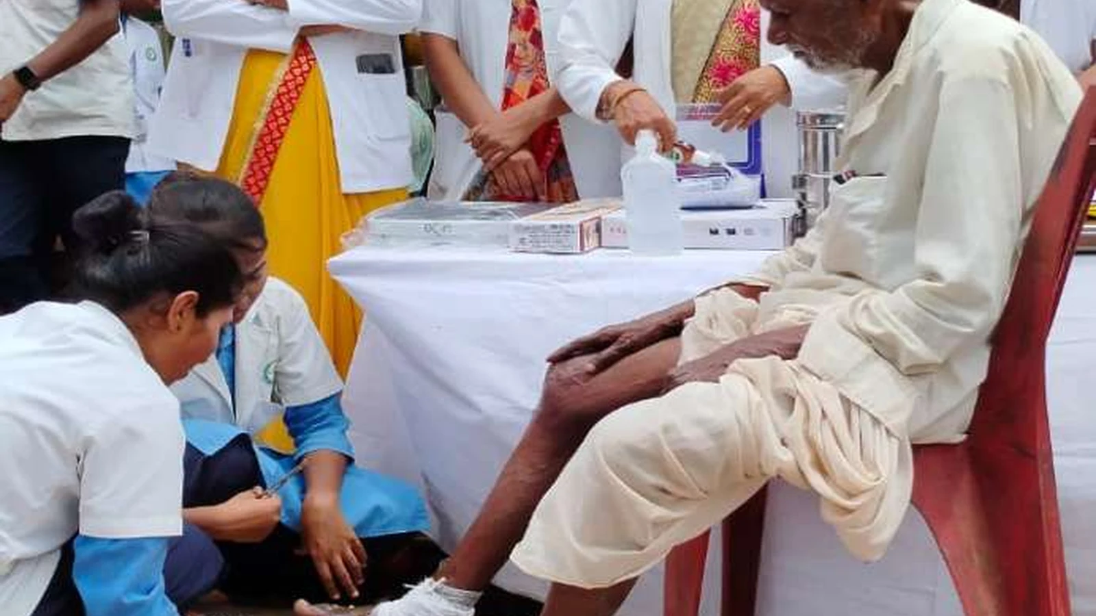 Third year BSc Nursing student of BLDEAS College of Nursing Jamkhandi performing sterile wound dressing on foot of elderly male resident seated on a chair at Jain Vrudhrashram Jamkhandi with other nursing students observing July 18 2024