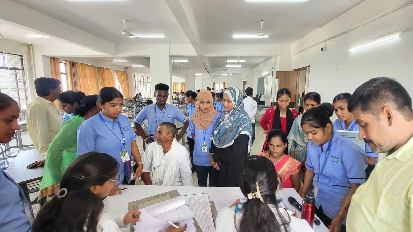 Students faculty and parents engaged in interactive discussion around classroom tables reviewing academic performance records during Parent-Teacher Meeting BLDEA College of Nursing Jamkhandi June 2026