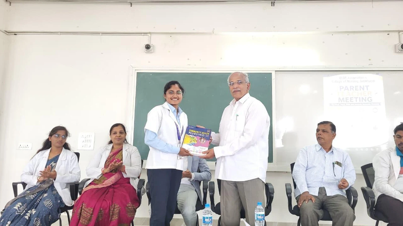 Prof S H Lagali Administrative Officer BLDE Association presenting textbook to college topper nursing student at BLDEA College of Nursing Jamkhandi during Parent-Teacher Meeting prize distribution ceremony June 2026