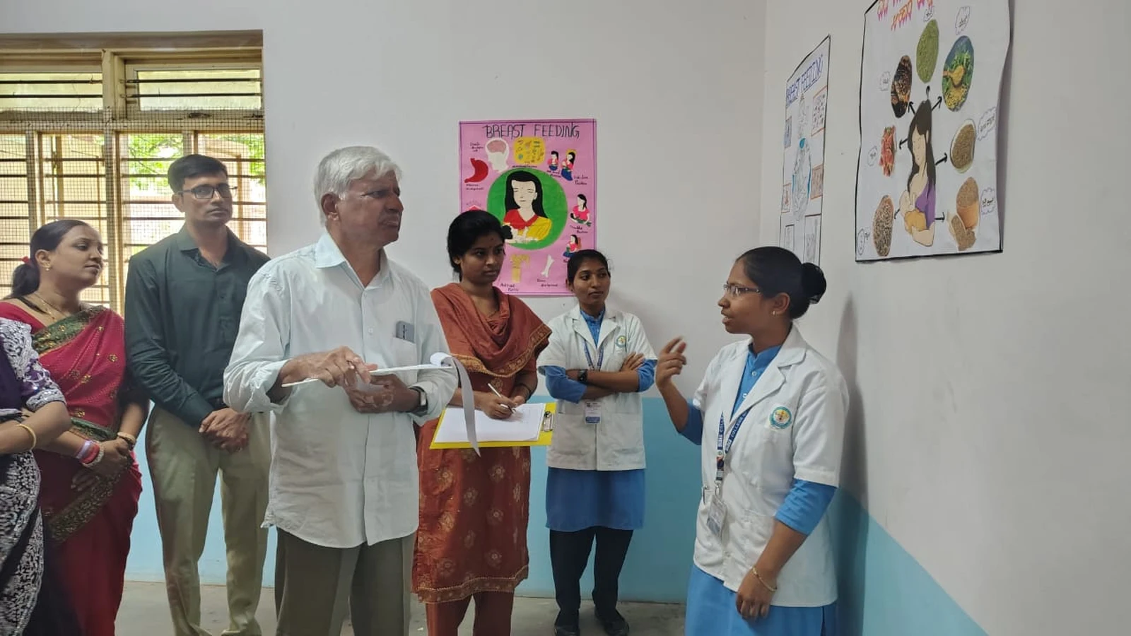 Dr H G Daddi judge and faculty evaluating BREAST FEEDING themed poster presented by BSc Nursing student in white coat at World Breastfeeding Week Poster Competition BLDEAS College of Nursing Jamkhandi August 7 2024