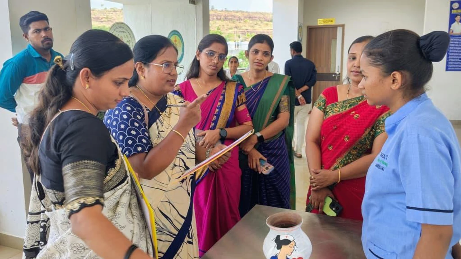 Judges evaluating a student's painted pot at Intercollegiate Pot Painting Competition 2026 – BLDEA College of Nursing Jamkhandi