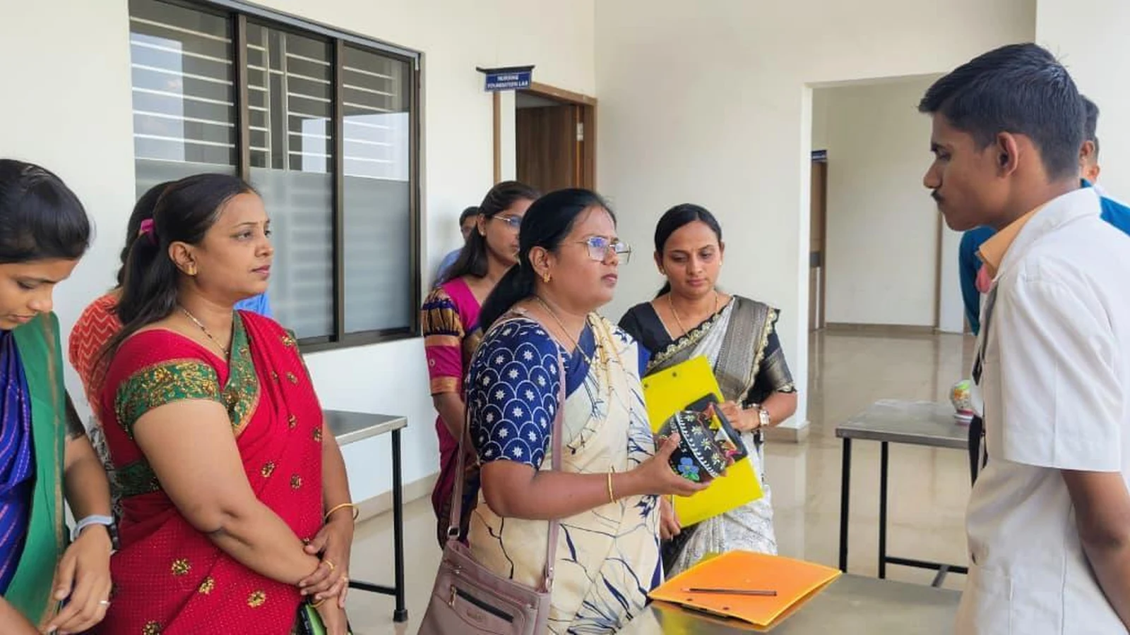 Judges reviewing a male student's pot painting at Intercollegiate Pot Painting Competition 2026 – BLDEA College of Nursing Jamkhandi
