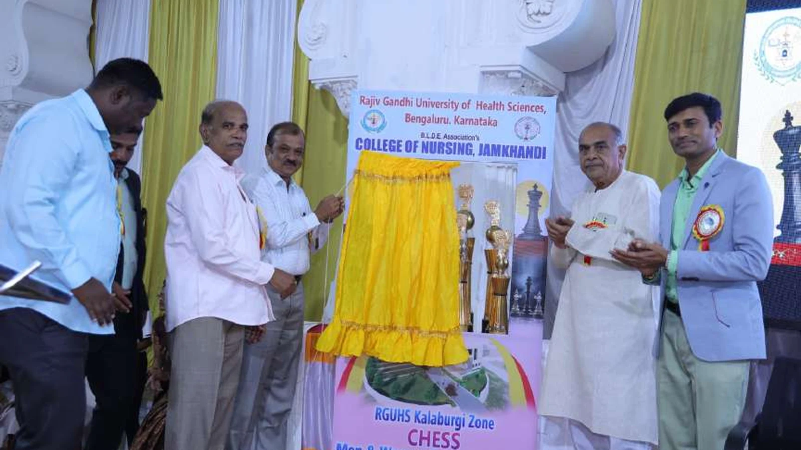 Dignitaries and organizers posing with trophies in front of RGUHS Kalaburagi Zone Chess Men and Women Tournament 2024 banner at Darbar Hall BLDEA Campus Jamkhandi with chess trophies and BLDEAS College of Nursing backdrop August 2024