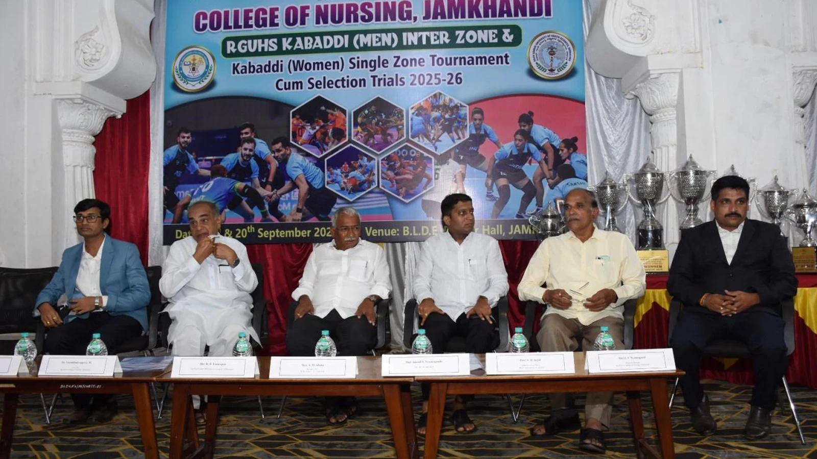 Dignitaries including Shri Anand S Nyamagouda Ex MLA Jamkhandi and Shri A M Shaha Chairman BLDE Association seated at dais with RGUHS Kabaddi Men Inter Zone and Women Single Zone Tournament 2025-26 banner at BLDEA College of Nursing Jamkhandi Darbar Hall