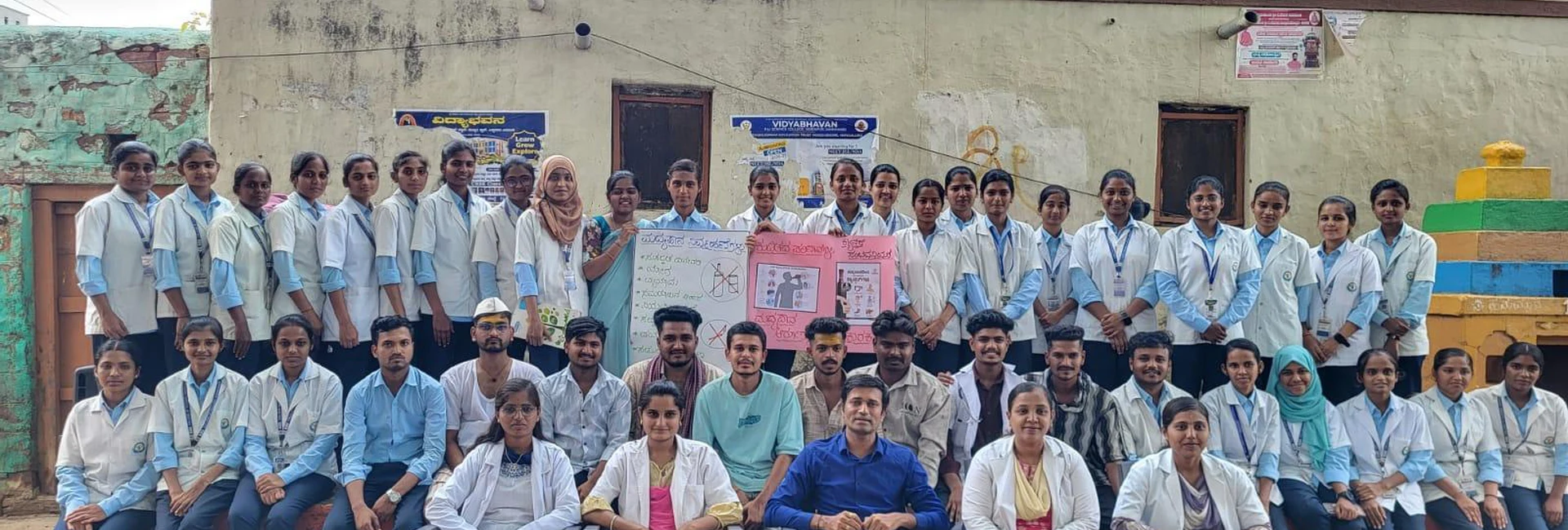 Seventh Semester BSc Nursing students BLDEA College of Nursing Jamkhandi full group photo with faculty and health education chart after Drug Addiction Awareness Role Play at Kakanwadi Village June 2026