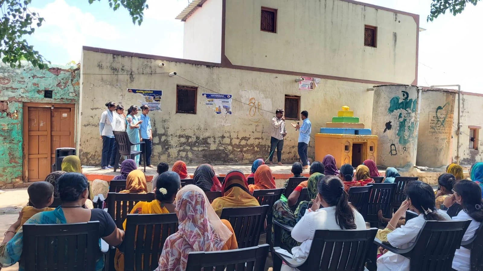 Wide view of Kakanwadi Village audience seated watching Fifth Semester BSc Nursing students BLDEA College of Nursing Jamkhandi perform Tobacco and Alcohol Prevention role play during Community Health Nursing activity June 2026