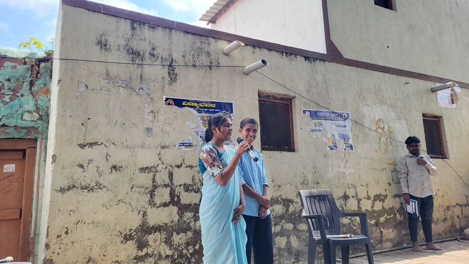 Fifth Semester BSc Nursing female students BLDEA College of Nursing Jamkhandi holding microphone performing Tobacco and Alcohol Prevention role play at Kakanwadi Village with male student alongside June 2026