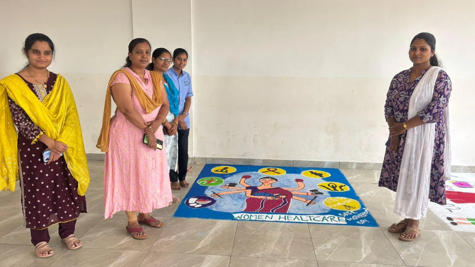 Student standing with Women Healthcare themed rangoli at National Safe Motherhood Day Rangoli Competition 2026 – BLDEA College of Nursing Jamkhandi