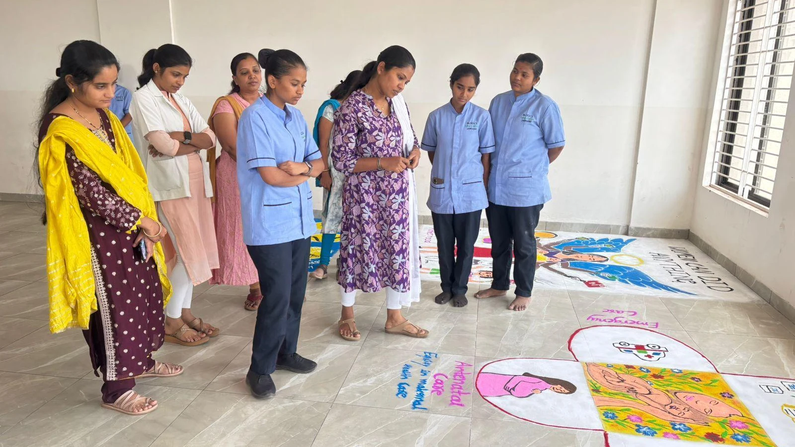 Judge and students evaluating maternal health rangoli designs at National Safe Motherhood Day 2026 – BLDEA College of Nursing Jamkhandi