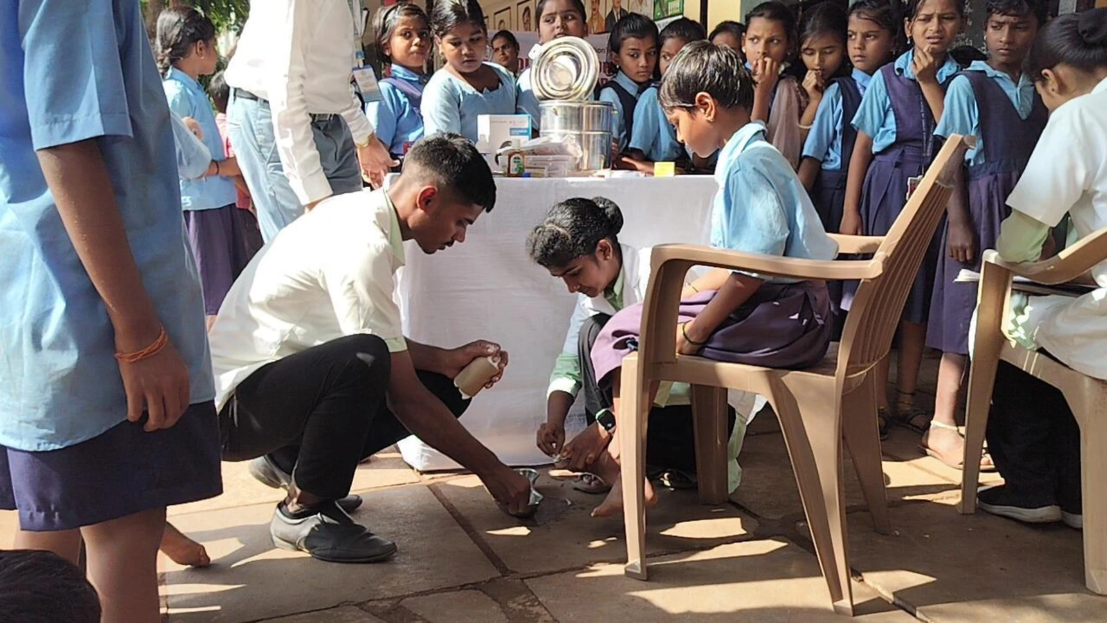 Male nursing student from BLDEAS College of Nursing Jamkhandi providing foot and wound care to a school child seated on chair during School Health Program at Government Primary School Mareguddi June 13 2025