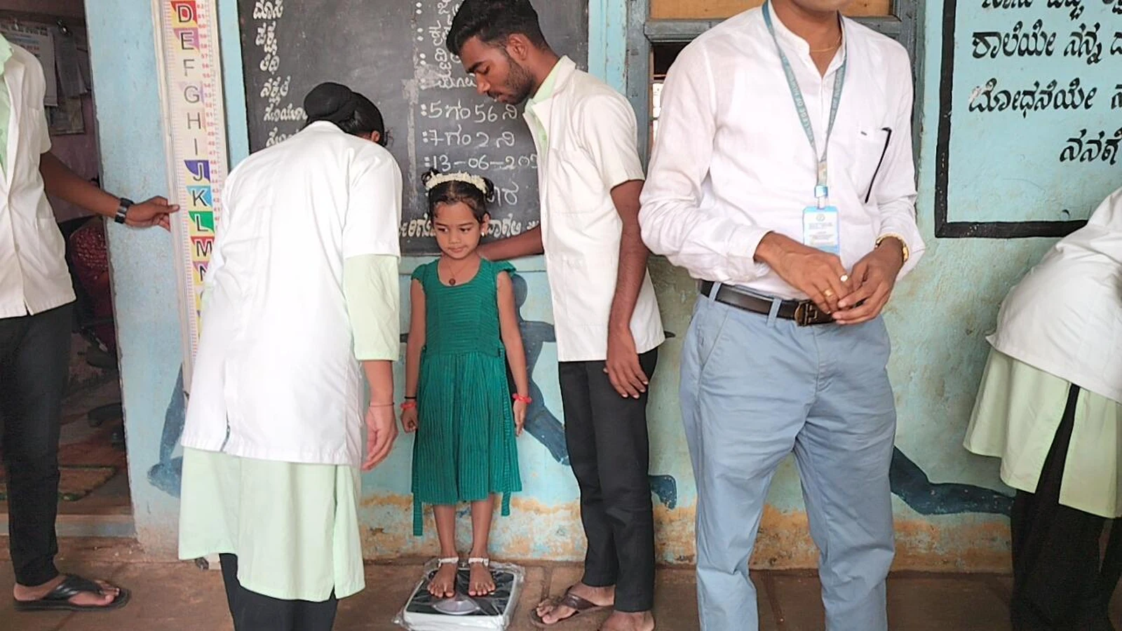 Two nursing students from BLDEAS College of Nursing Jamkhandi weighing a girl child on weighing scale during anthropometric assessment School Health Program at Government Primary School Mareguddi June 13 2025