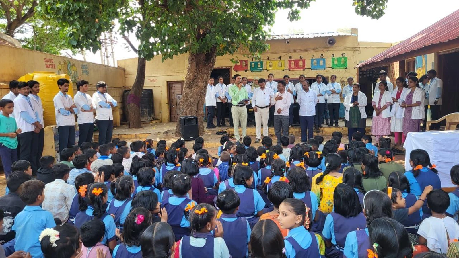 Dr Veerabhadrappa G Mendagudli Principal BLDEA College of Nursing Jamkhandi addressing school children assembled in courtyard at Government Primary School Kakanwadi during School Health Programme inauguration June 2026