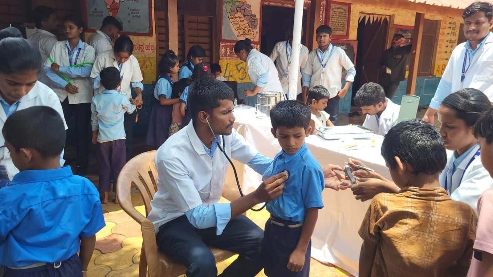 BSc Nursing student BLDEA College of Nursing Jamkhandi performing physical examination with stethoscope on school child during health screening at Government Primary School Kakanwadi School Health Programme June 2026
