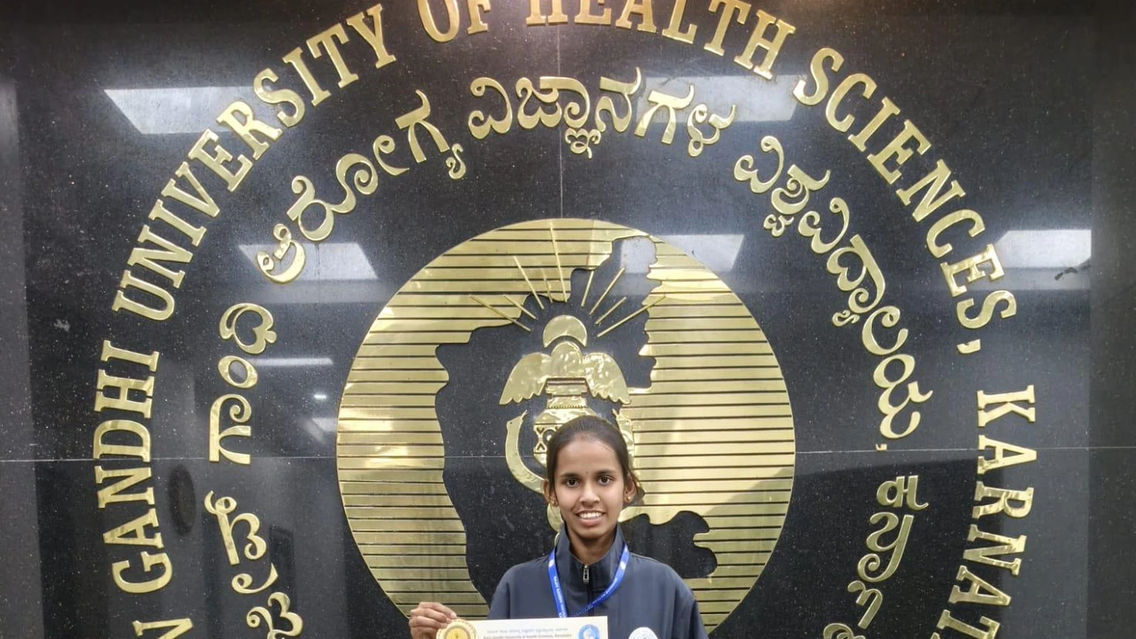 Ms. Kaveri Ramesh Sonnad BSc Nursing BLDEA Jamkhandi displaying University Blue Honour certificate in RGUHS sports tracksuit at RGUHS Bengaluru lobby