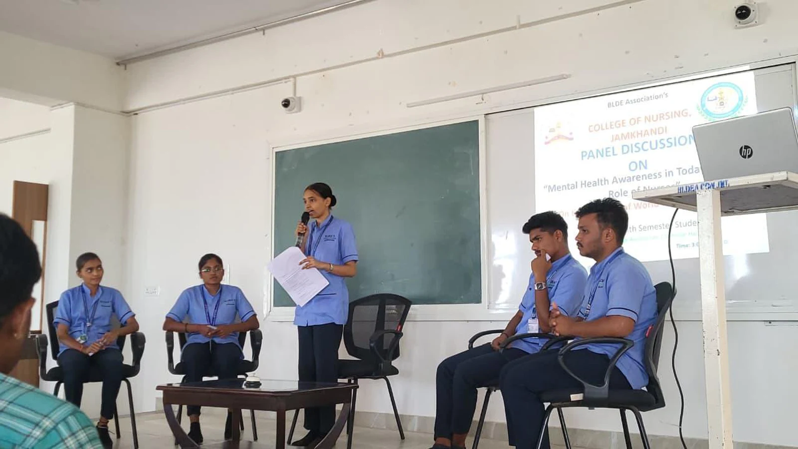 Moderator Ms. Ankita addressing audience with panelists seated at World Health Day 2026 Panel Discussion – BLDEA College of Nursing Jamkhandi